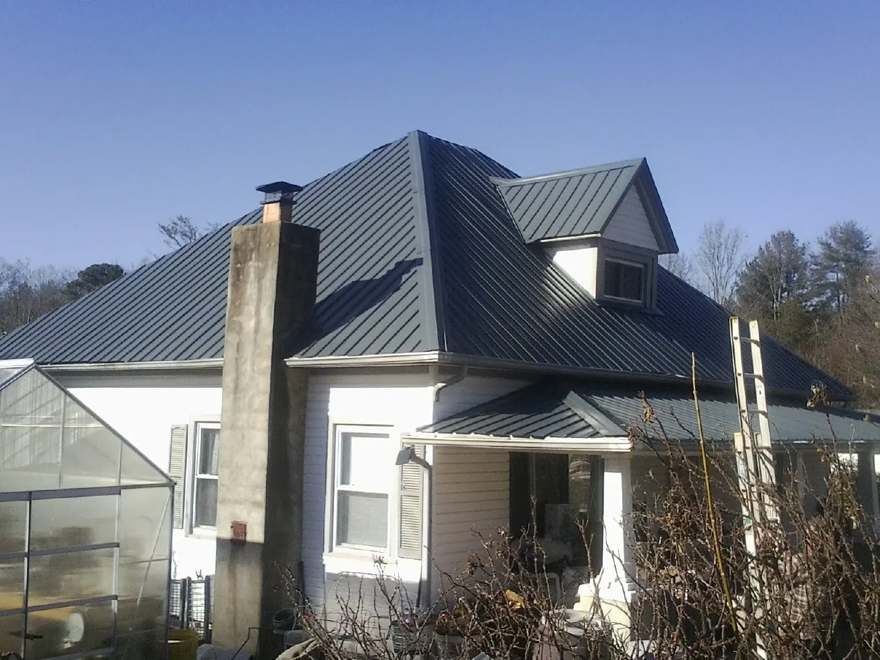 Dark blue standing seam metal roof on a white farmhouse with dormer — Slate & Tile Roof Repair by Roofing Brothers in Dale