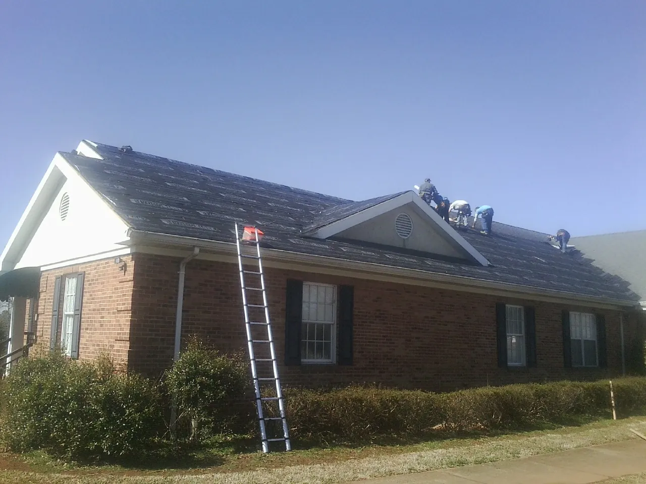 Crew tearing shingles off a brick ranch roof with a ladder set — Metal Roof Repair work by our crew in Dale