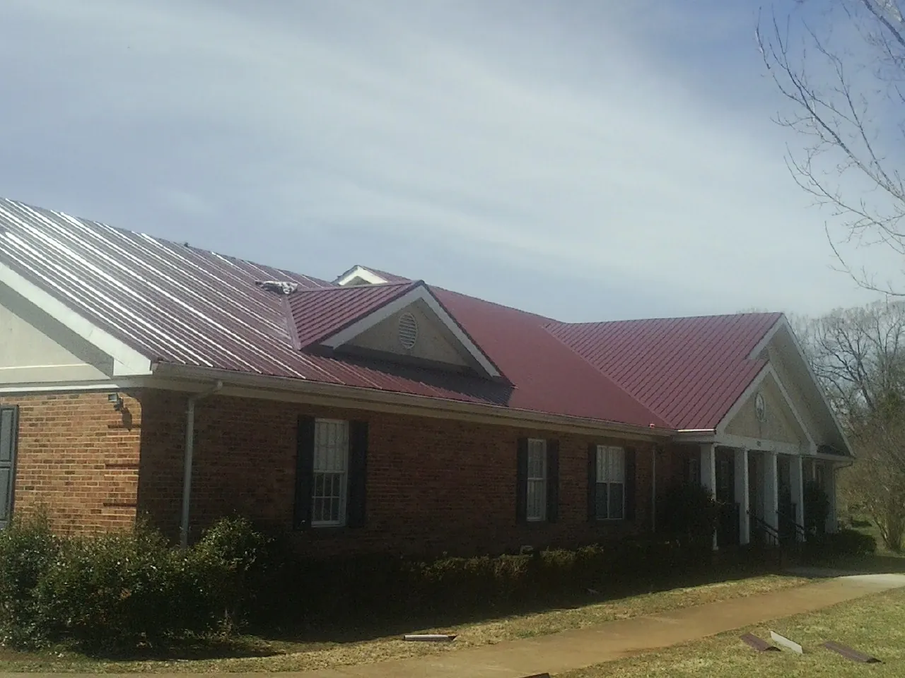 Red metal roof with gabled entries on a long brick building, from a Hail Damage Roof Repair job in Dale